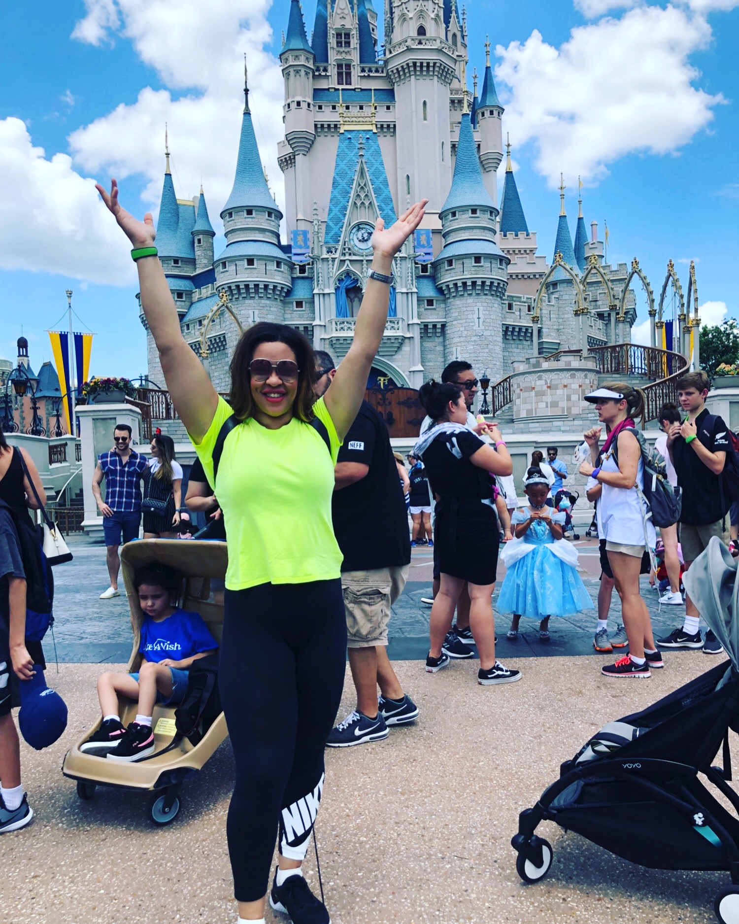 Photo of LMS in a neon yellow top and Nike tights, hands raised in front of Cinderella castle at DisneyWorld.